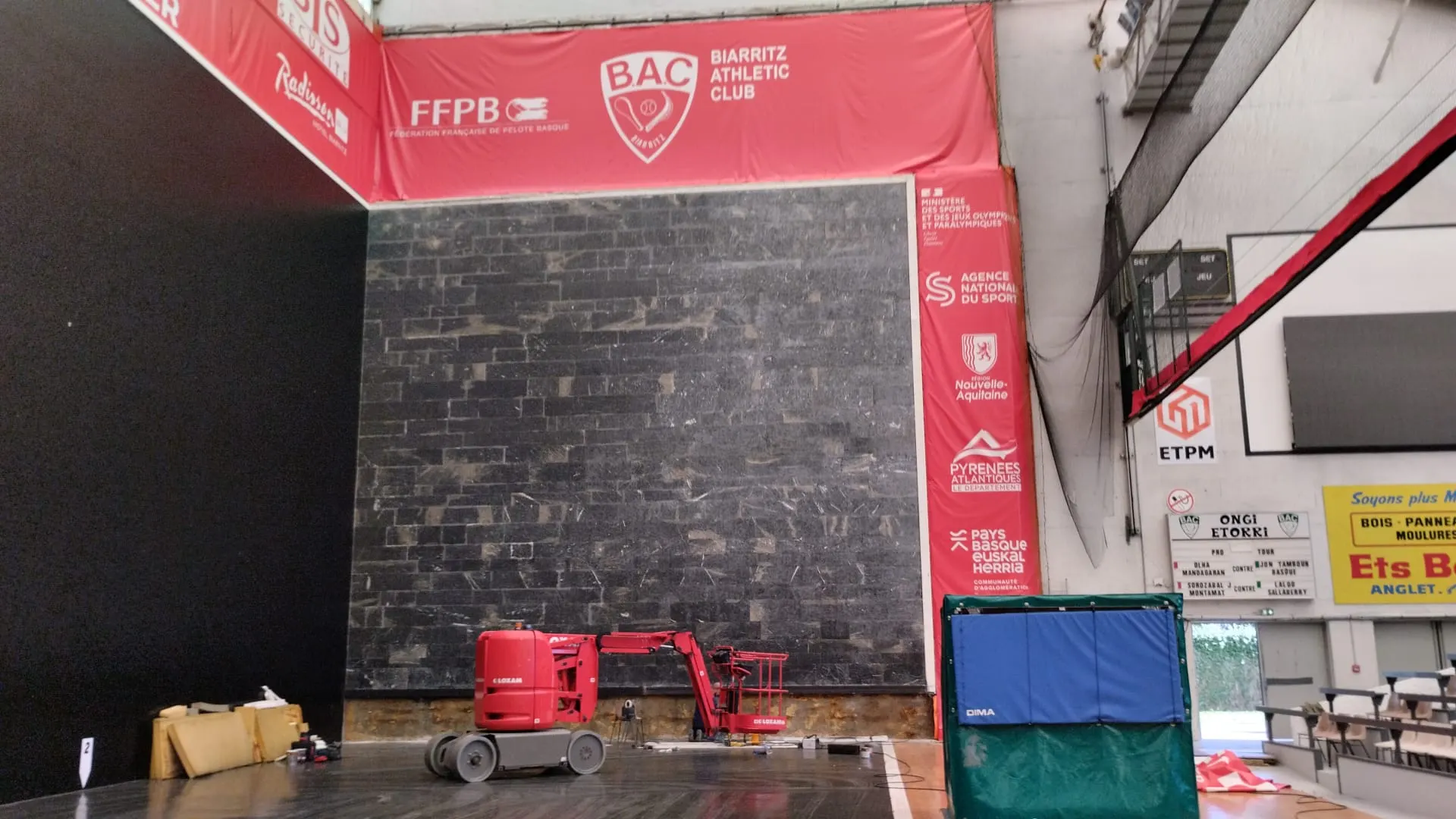 Frontón cubierto del Biarritz Athletic Club con muro de piedra oscura y plataforma elevadora roja en mantenimiento