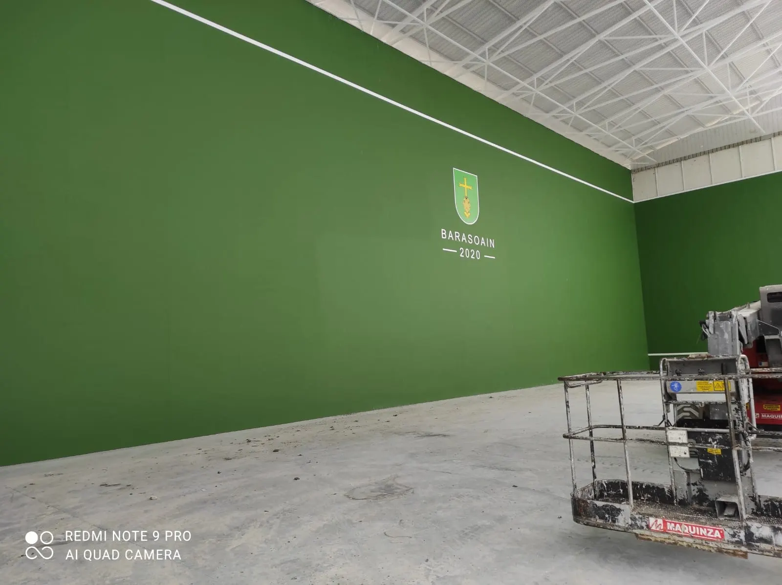Frontón cubierto con paredes pintadas de verde y escudo de Barasoain 2020, con una plataforma elevadora en primer plano