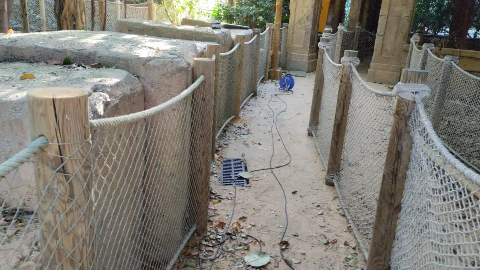 Pasillo vallado con postes de madera, cuerda y red de protección, con un cable eléctrico en el suelo durante una reparación
