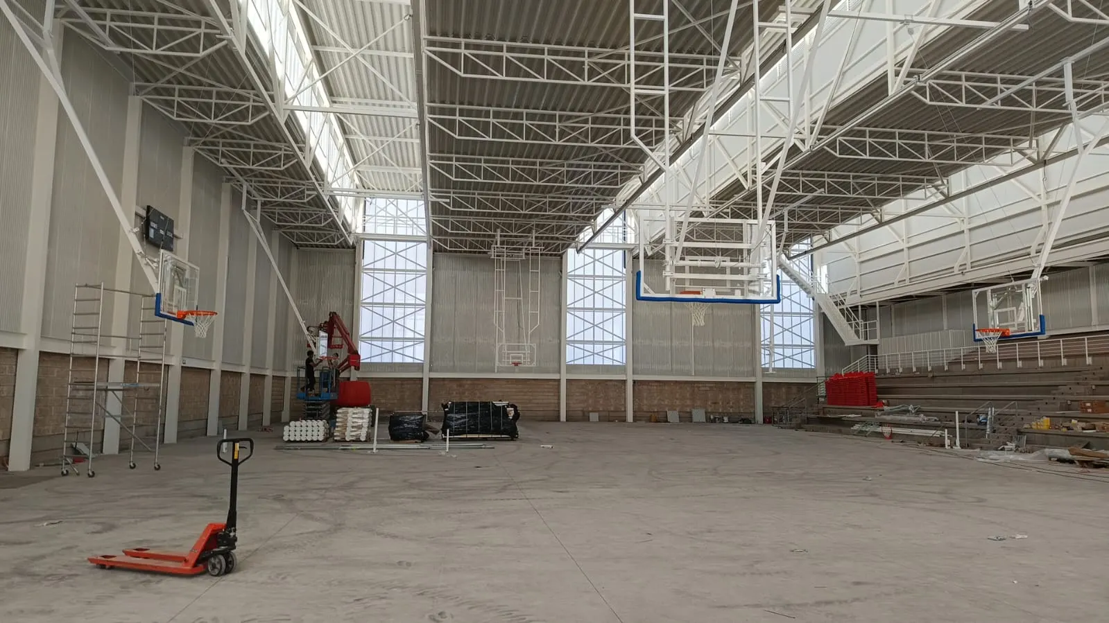 Montaje de canastas de baloncesto abatibles a techo en un pabellón en obras, con plataforma elevadora y gradas