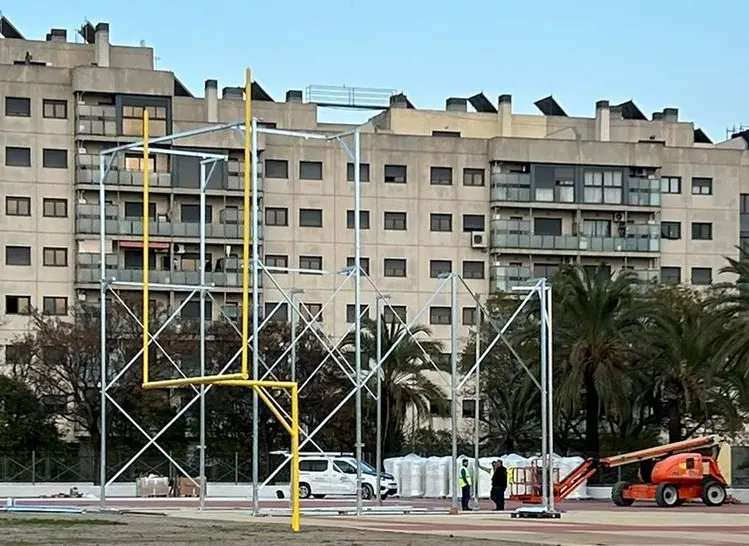 Montaje de una jaula de lanzamiento metálica junto a una portería amarilla en una pista de atletismo con operarios