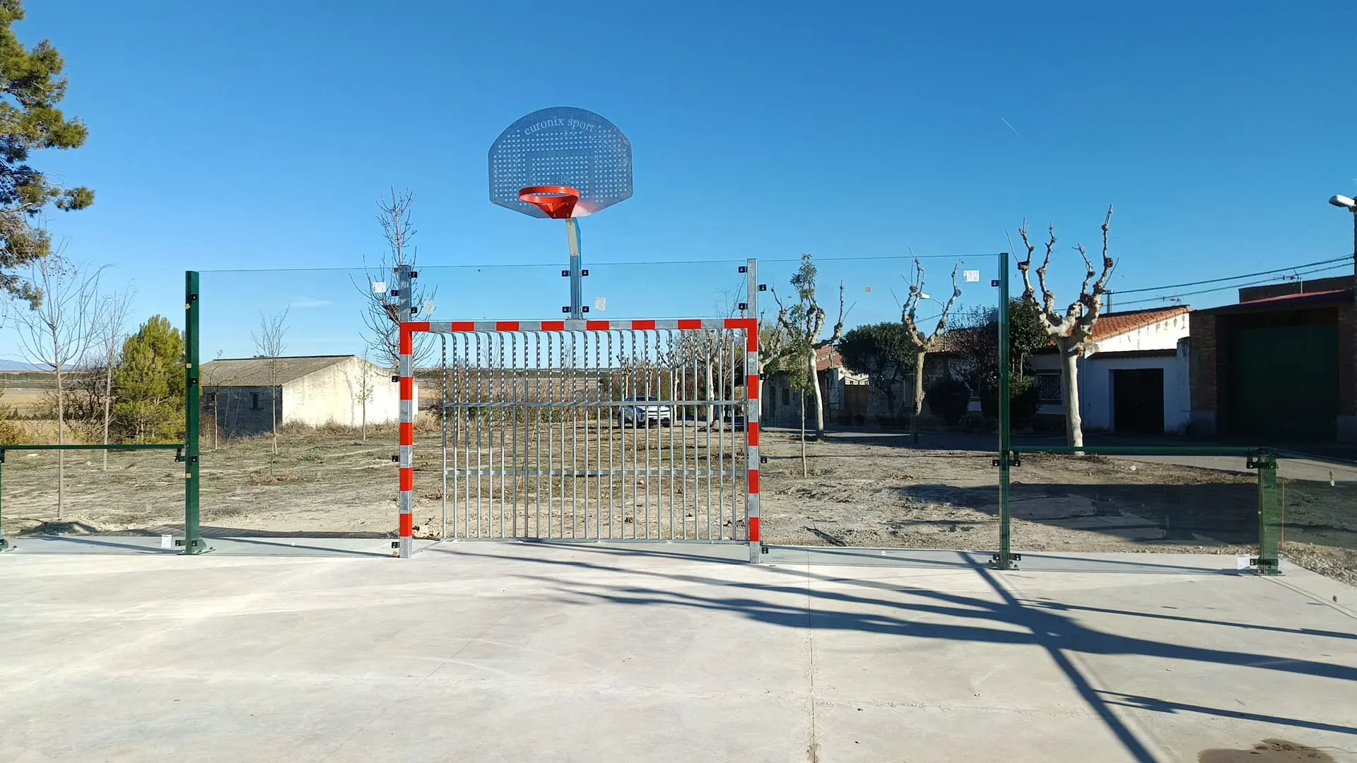 Montaje de portería antivandálica con red de barras metálicas y canasta en una pista de hormigón al aire libre