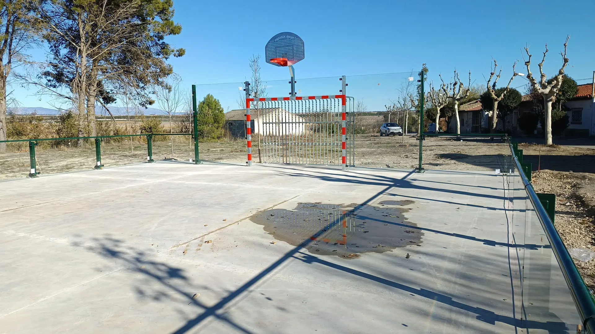 Instalación deportiva al aire libre con portería antivandálica roja y blanca, canasta y vallado de paneles transparentes