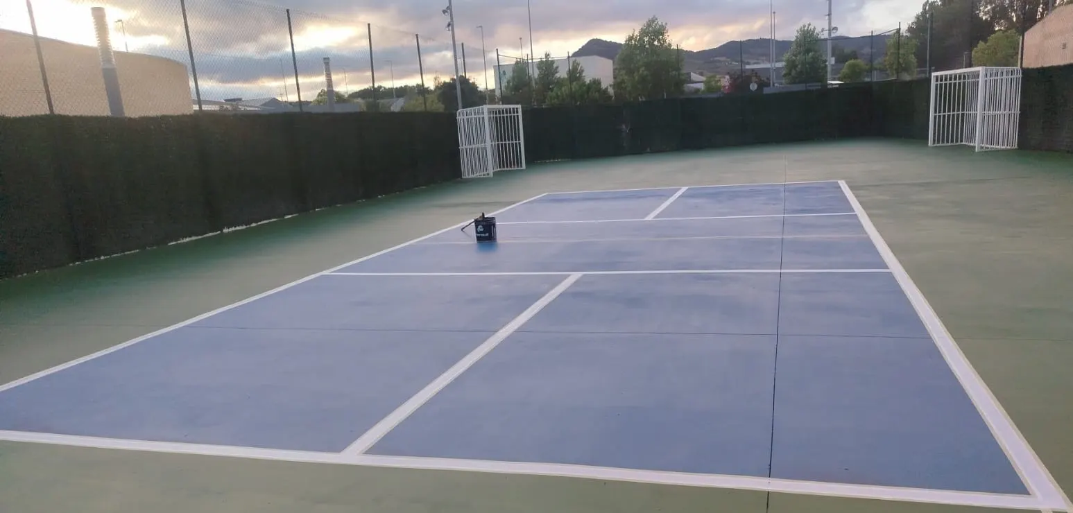 Pista deportiva exterior recién pintada en azul y verde con líneas blancas, porterías de fútbol sala y valla verde