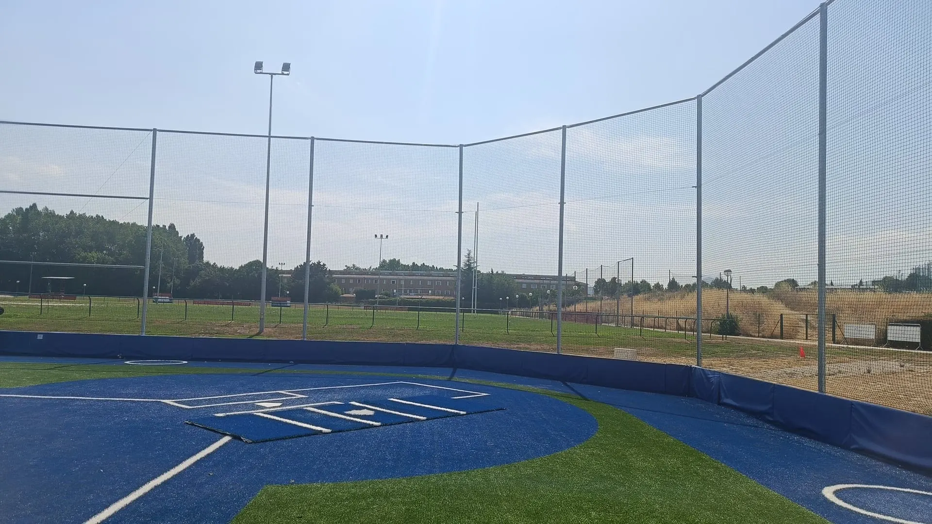 Red de protección sobre postes metálicos alrededor de un campo de béisbol con césped artificial azul y verde