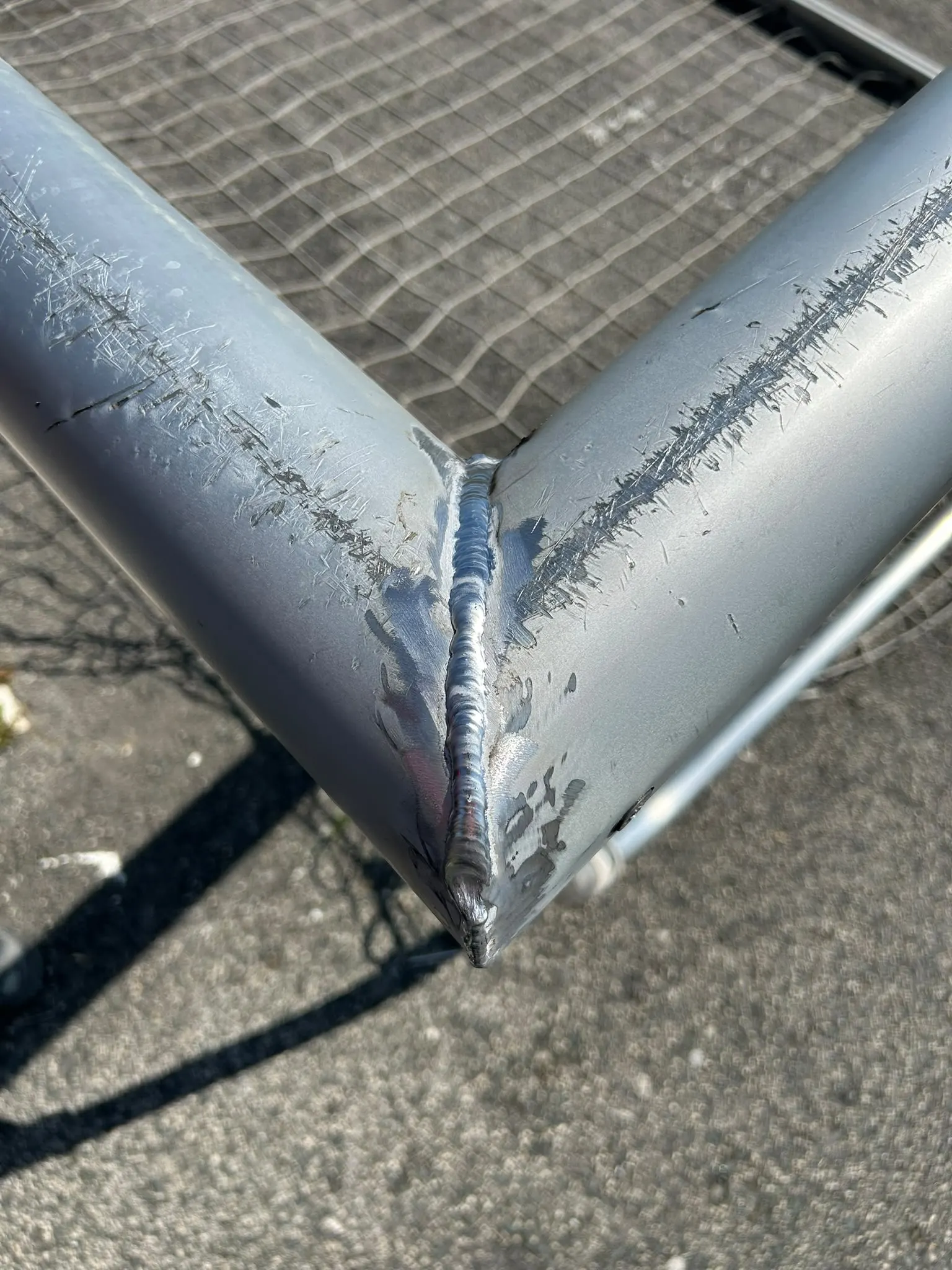 Cordón de soldadura en la esquina de una portería metálica rayada, reparada durante el mantenimiento, con la red detrás